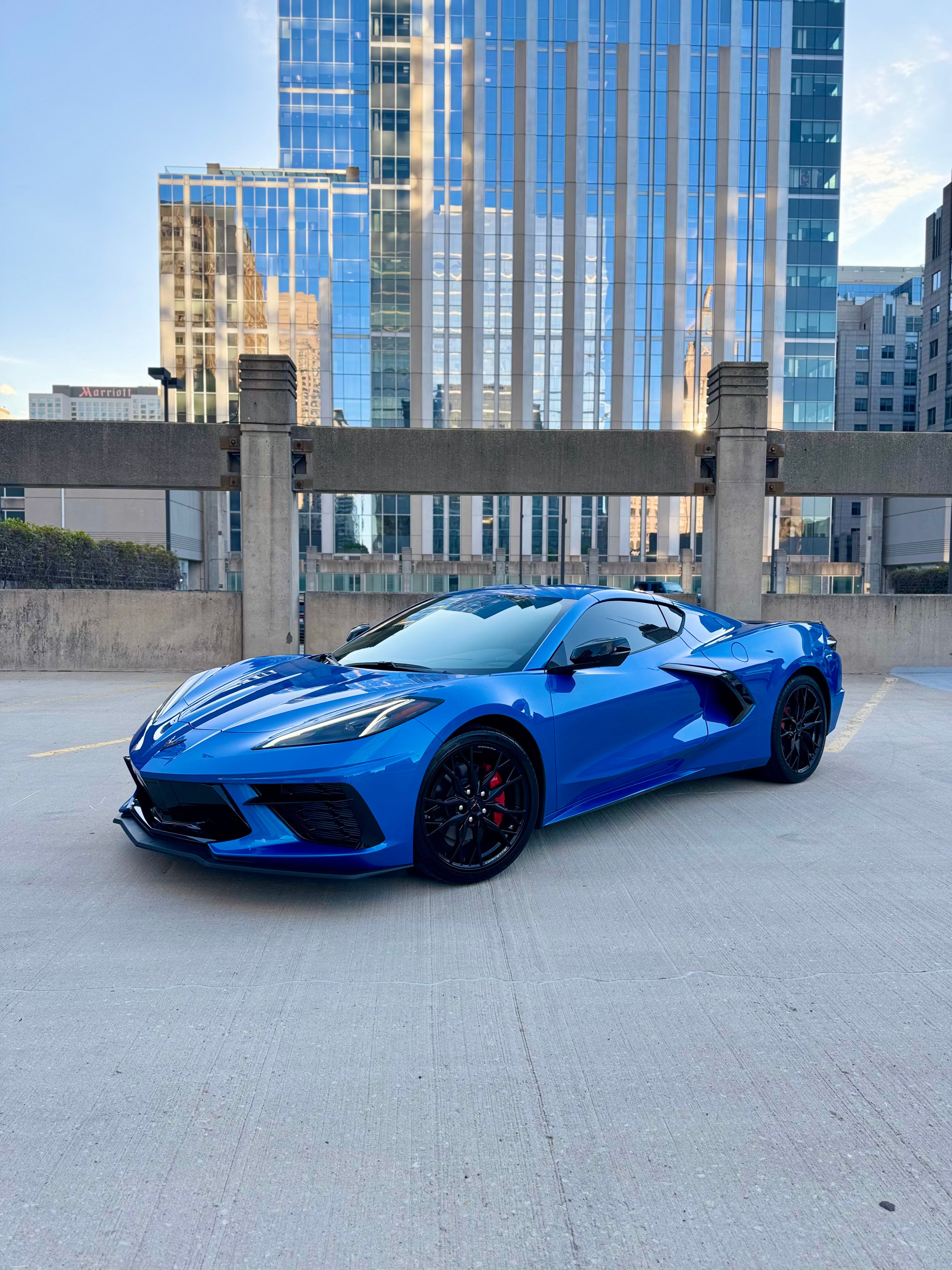 Bright blue C8 Corvette with black rims, parked on a rooftop against a backdrop of Chicago’s modern skyscrapers.